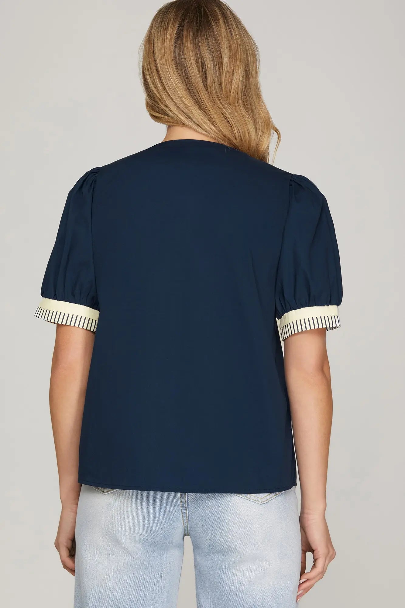 Navy blue blouse with white trim on sleeves and collar worn by a person on a plain background