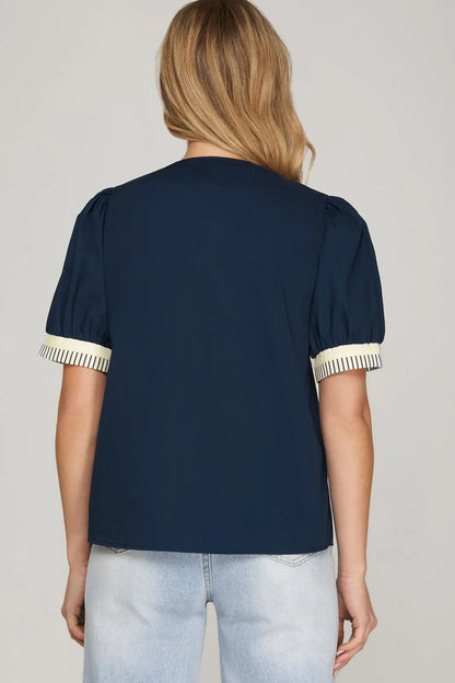 Navy blue blouse with white trim on sleeves and collar worn by a person on a plain background