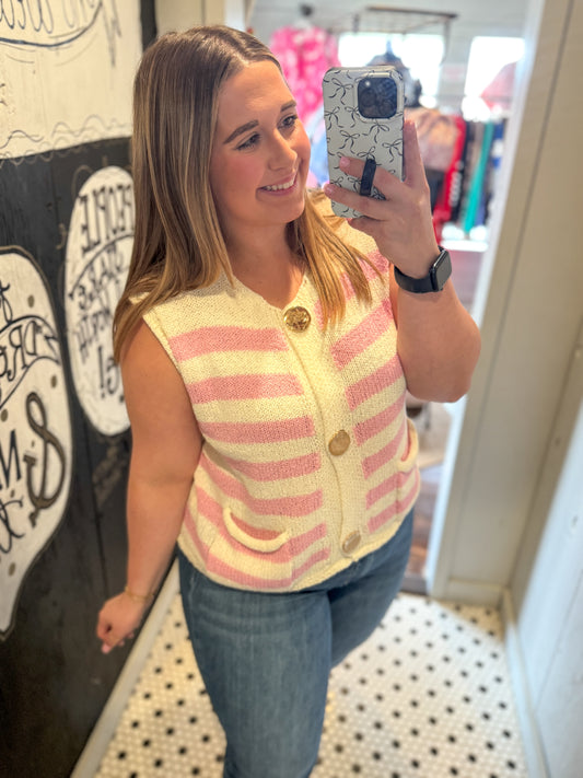 Woman taking a mirror selfie wearing a striped vest in a store.