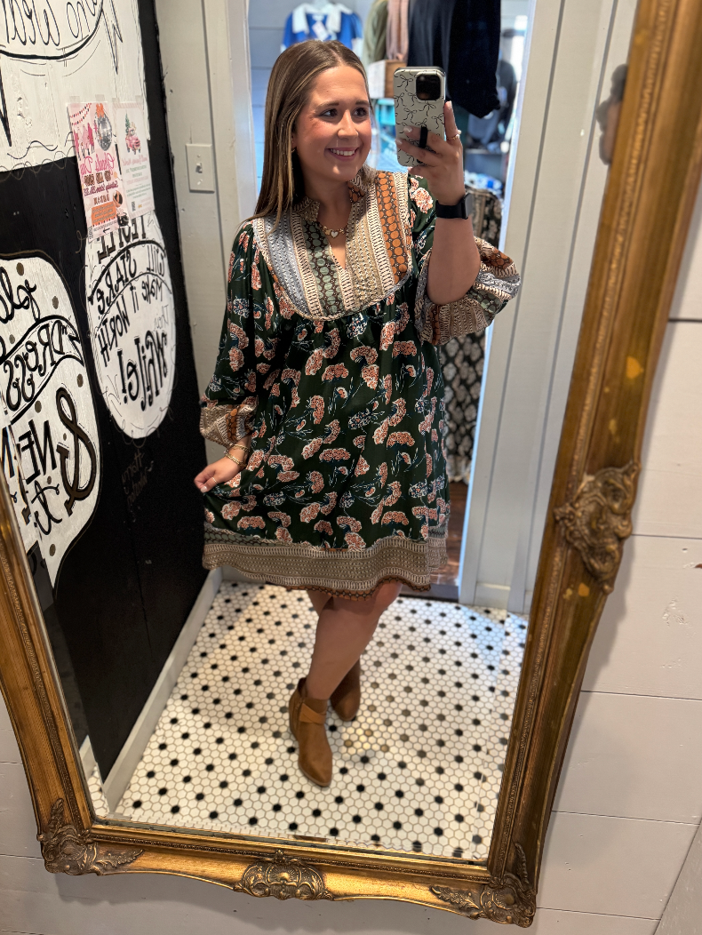 Woman taking a mirror selfie wearing a floral dress in a store.
