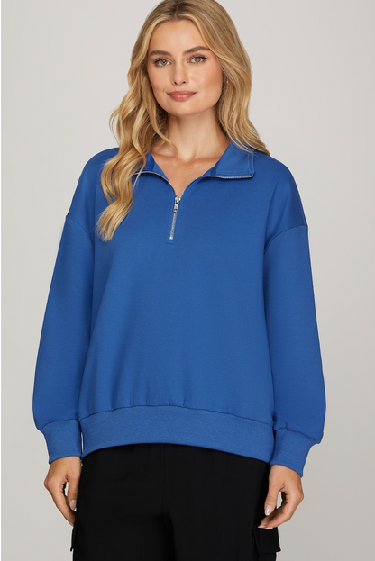 Woman wearing a blue zip-up sweatshirt against a plain background