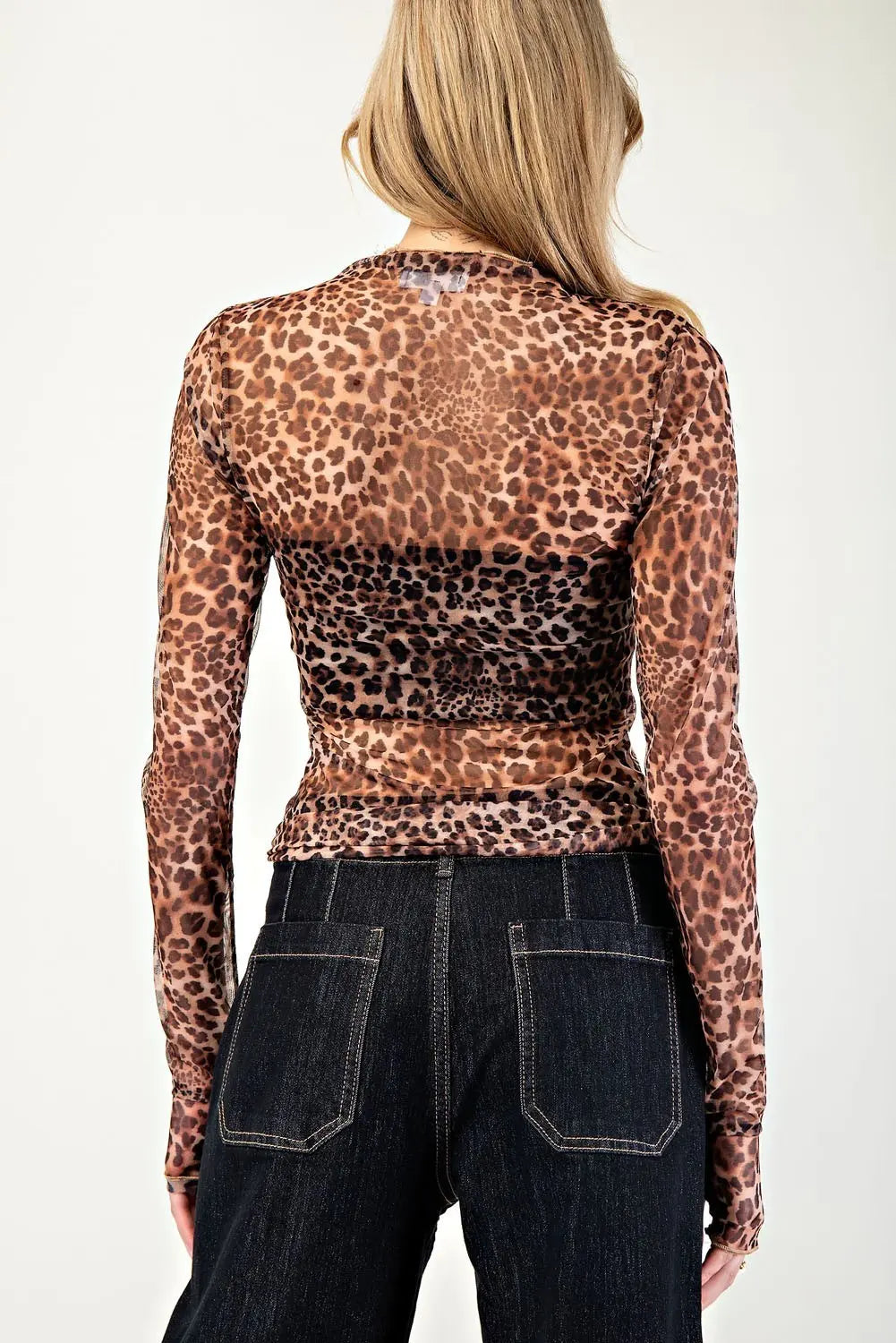 Person wearing a leopard print long-sleeve top and dark jeans on a plain background