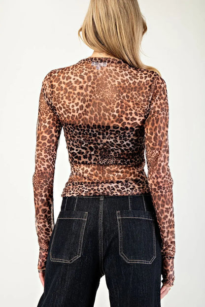 Person wearing a leopard print long-sleeve top and dark jeans on a plain background