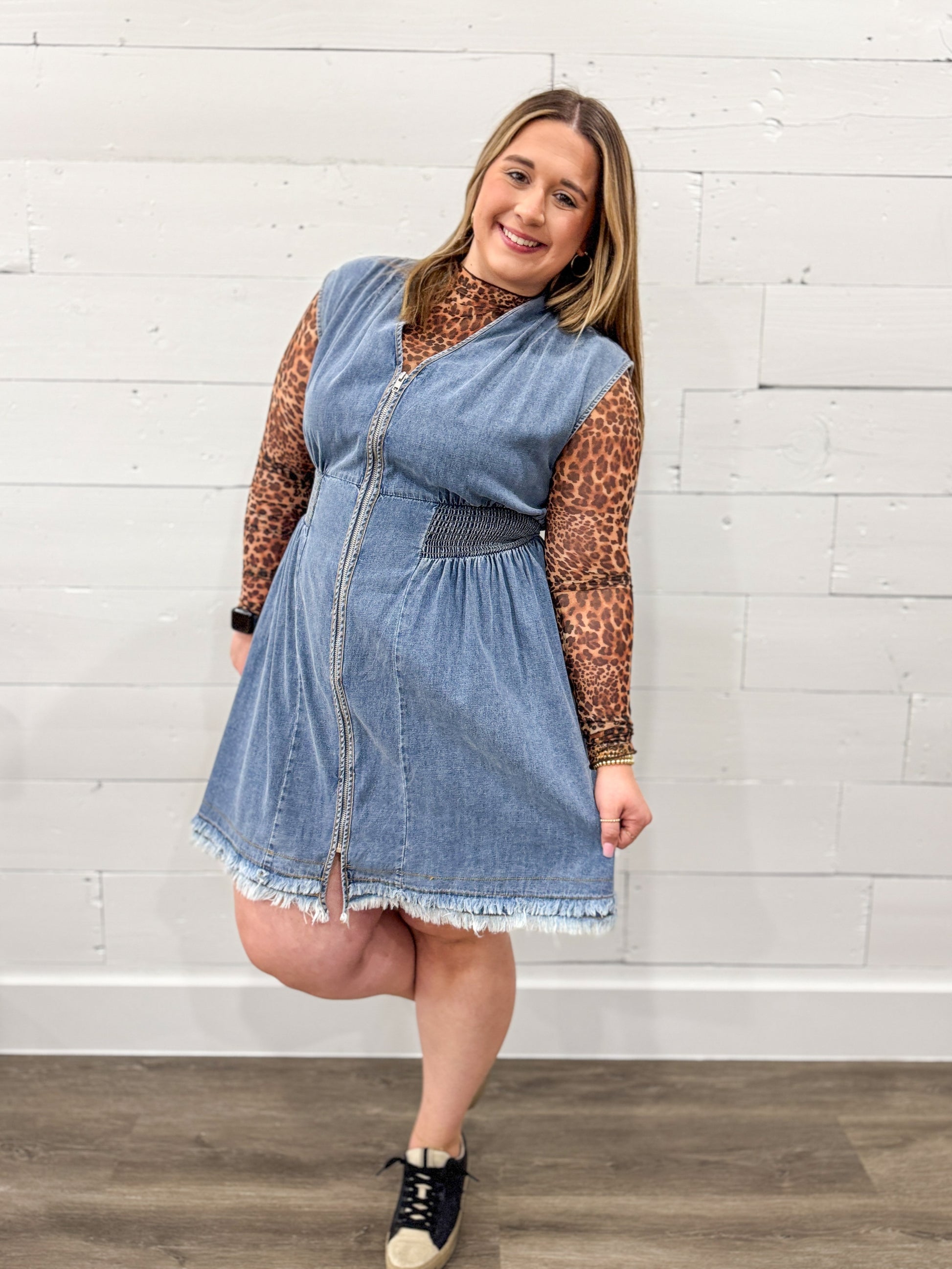 Woman wearing a denim dress with a white brick wall background