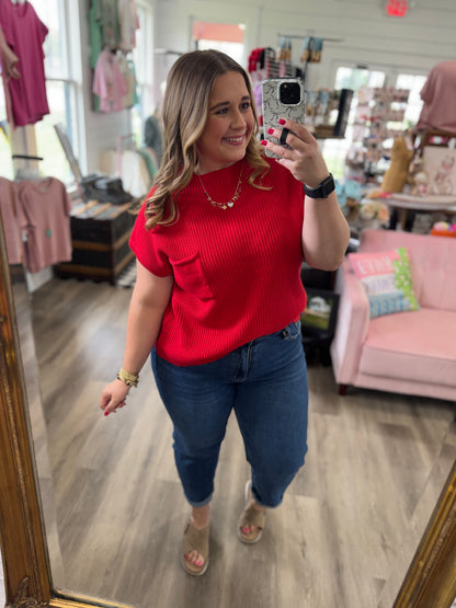 Woman taking a mirror selfie wearing a red top and blue jeans in a store.