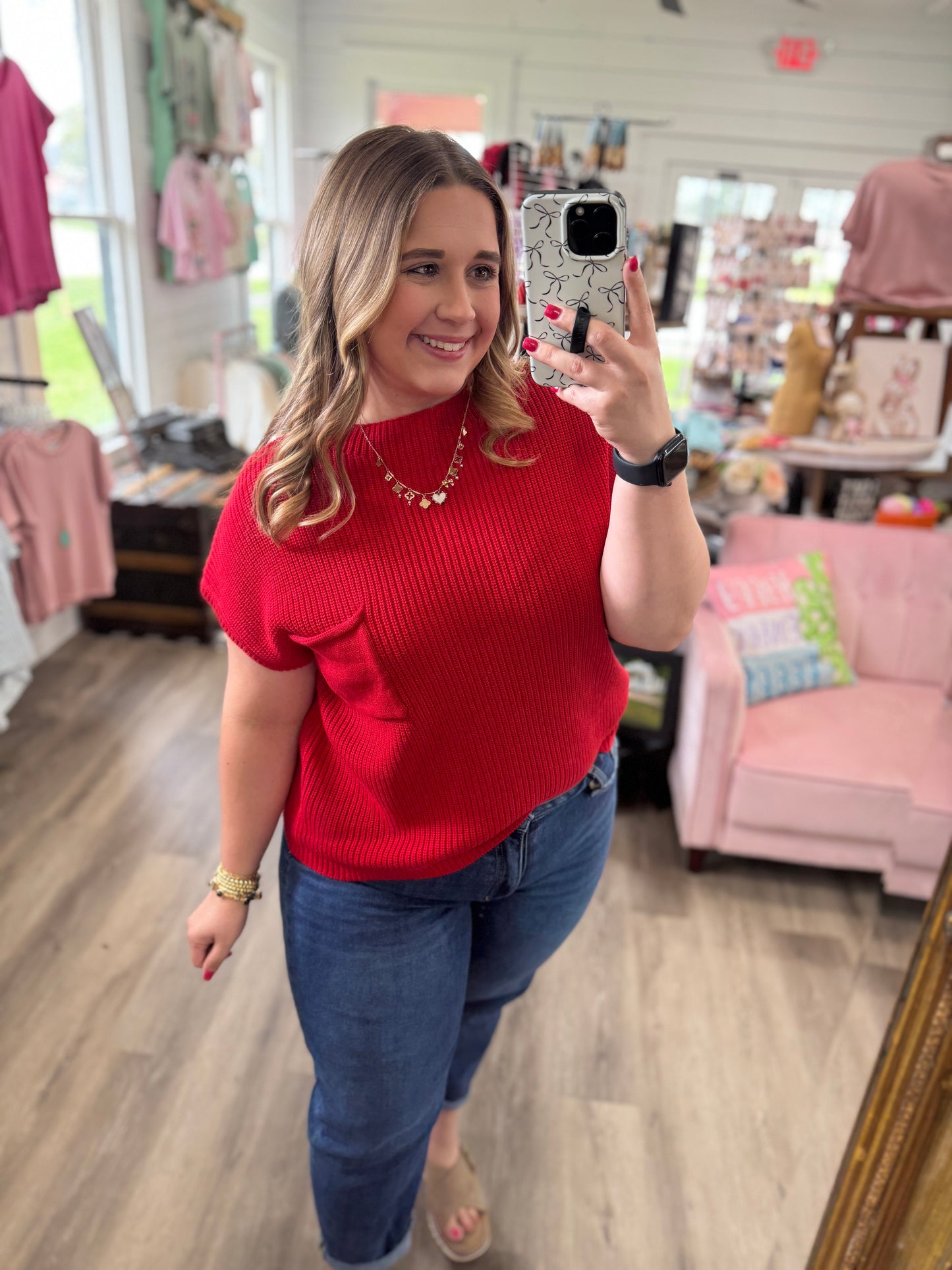 Woman taking a mirror selfie wearing a red sweater and blue jeans in a store.