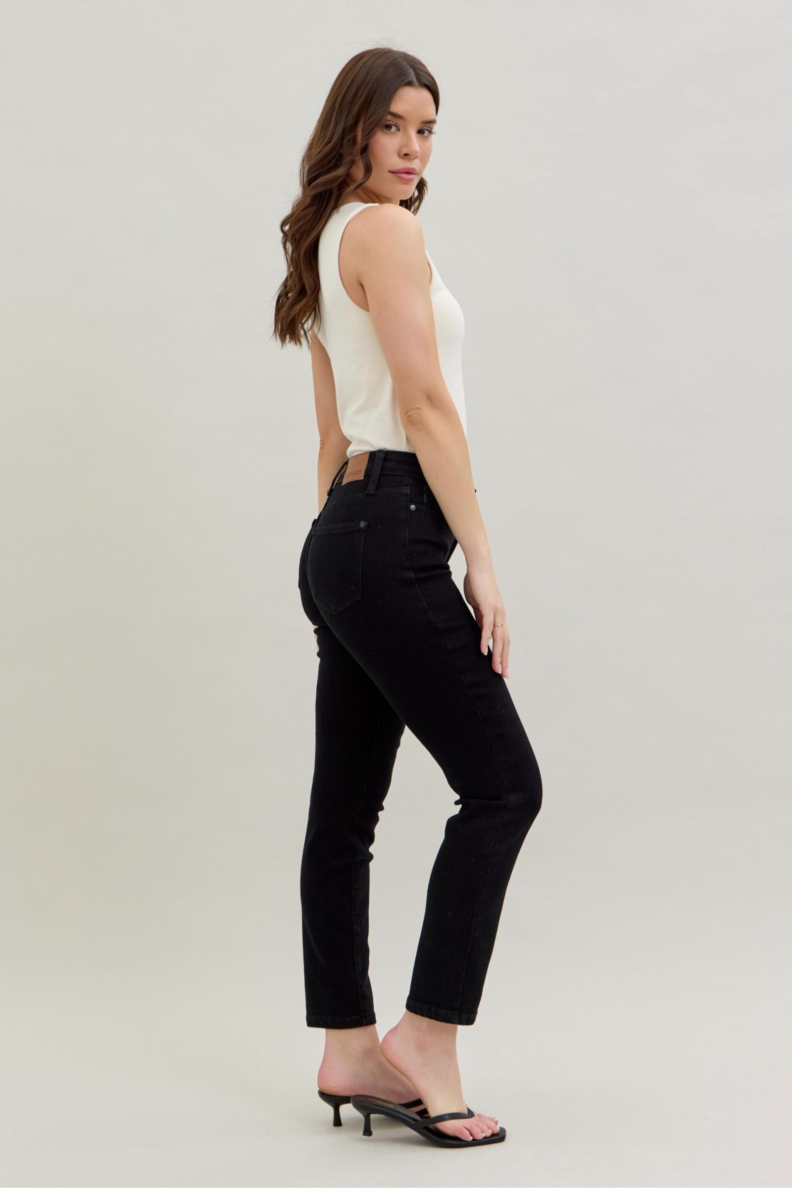 Woman wearing black pants and a white top on a plain background