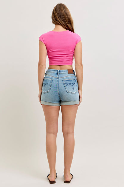 Person wearing a pink crop top and denim shorts on a plain background