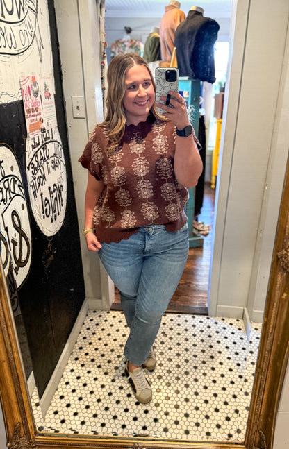 Woman taking a mirror selfie wearing a brown patterned sweater and blue jeans in a store.