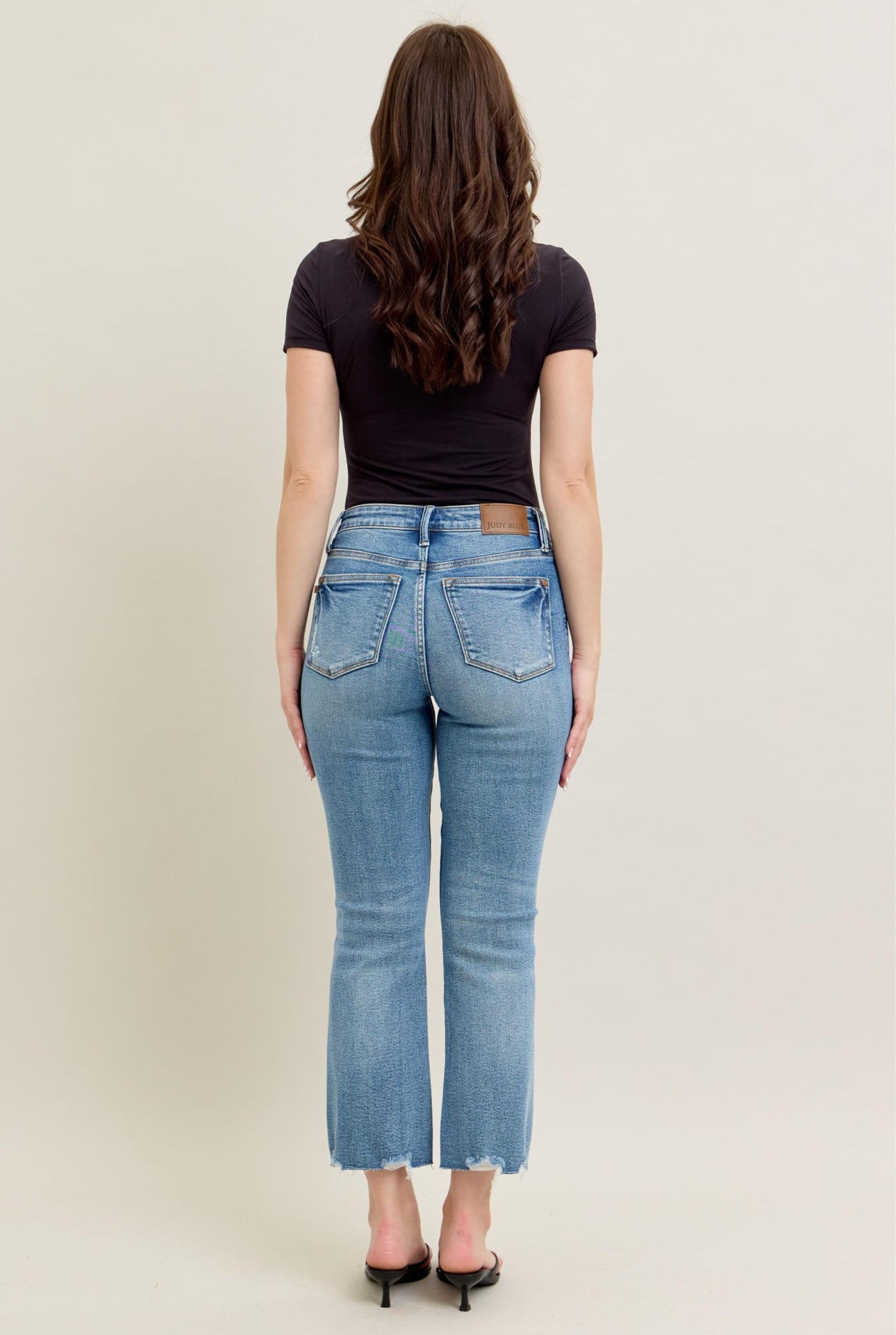Person wearing blue jeans and a black top on a plain background