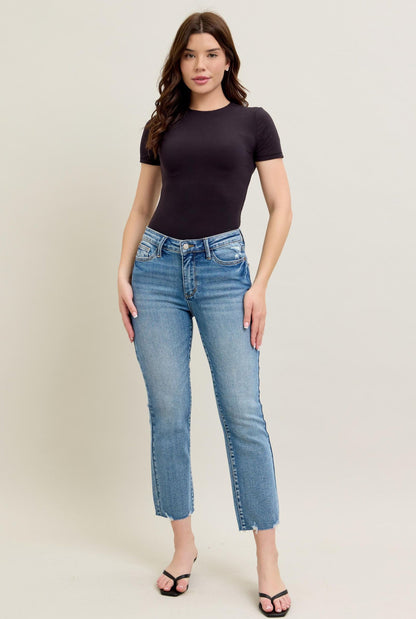 Woman wearing a black t-shirt and light blue jeans on a plain background