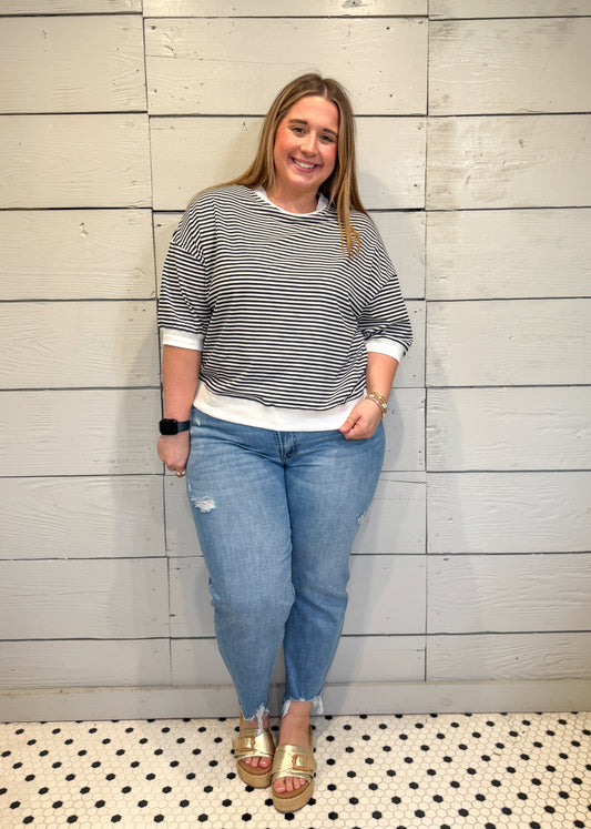 Woman wearing a striped sweater and jeans standing against a wooden paneled wall.