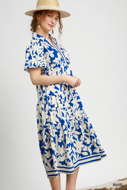 Woman wearing a blue and white floral dress with a straw hat on a plain background