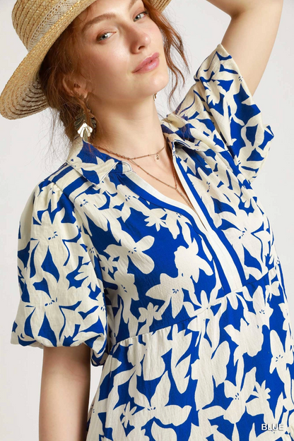 Woman wearing a blue and white floral dress with a straw hat on a light background