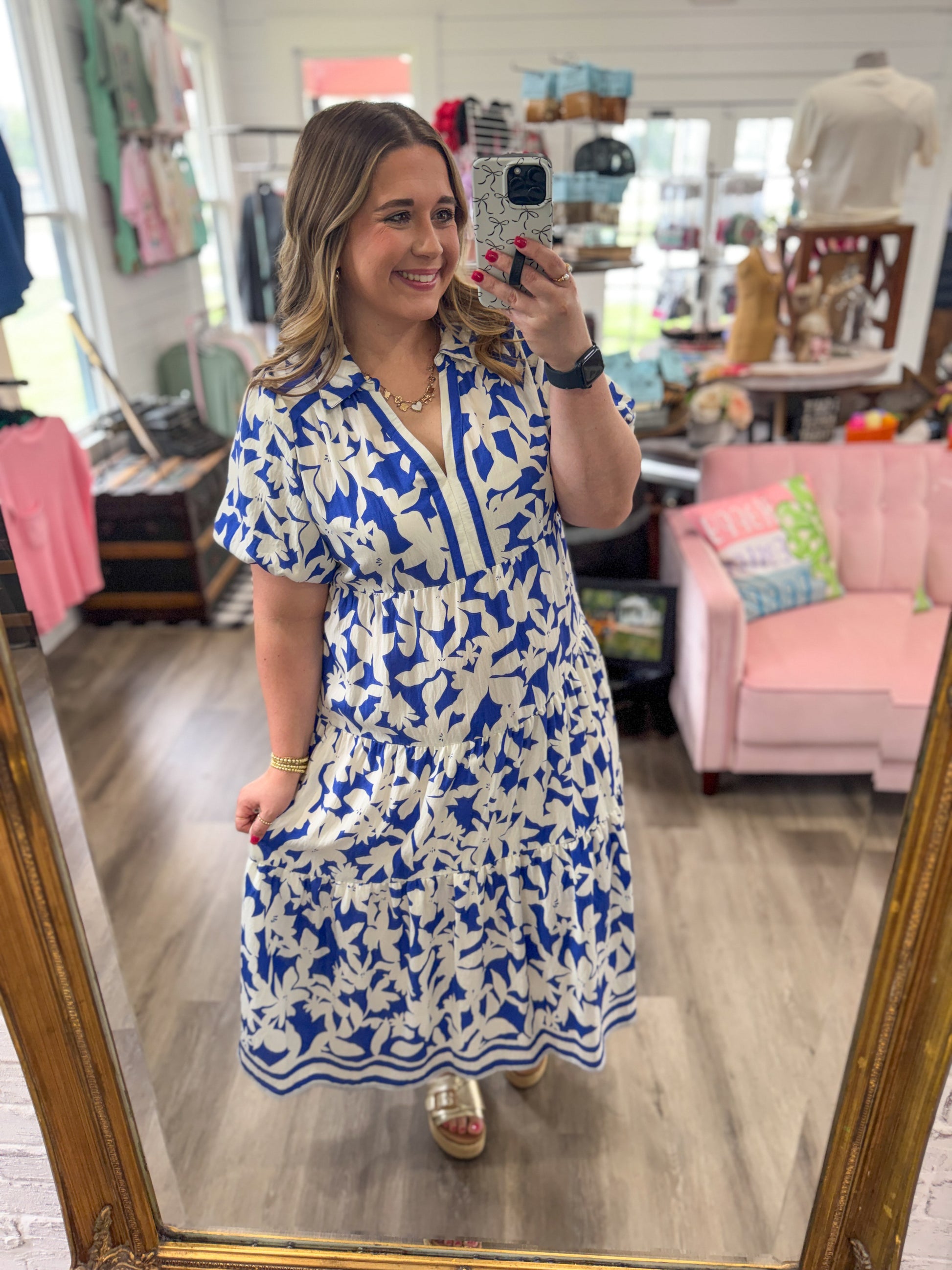 Woman taking a mirror selfie wearing a blue and white dress in a store.