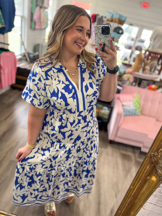 Woman taking a mirror selfie wearing a blue and white floral dress in a store.