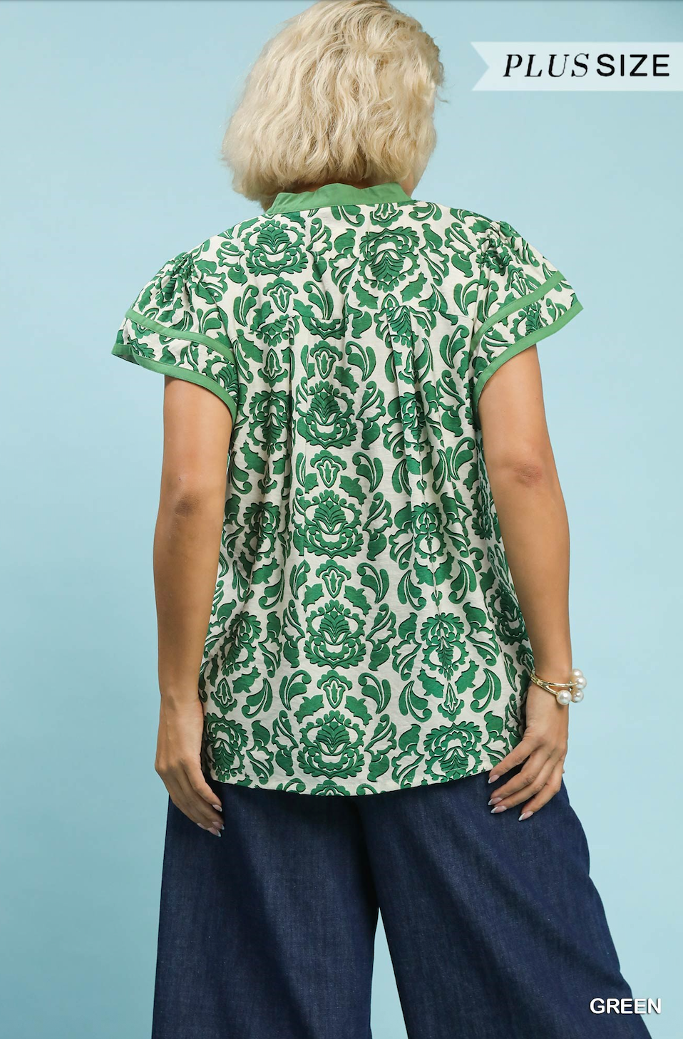 Woman wearing a green floral patterned blouse against a light blue background
