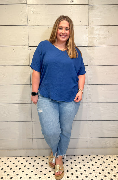 Woman wearing a blue top and jeans standing against a tiled wall.