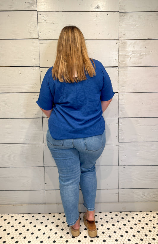 Person wearing a blue shirt and jeans standing against a tiled wall.