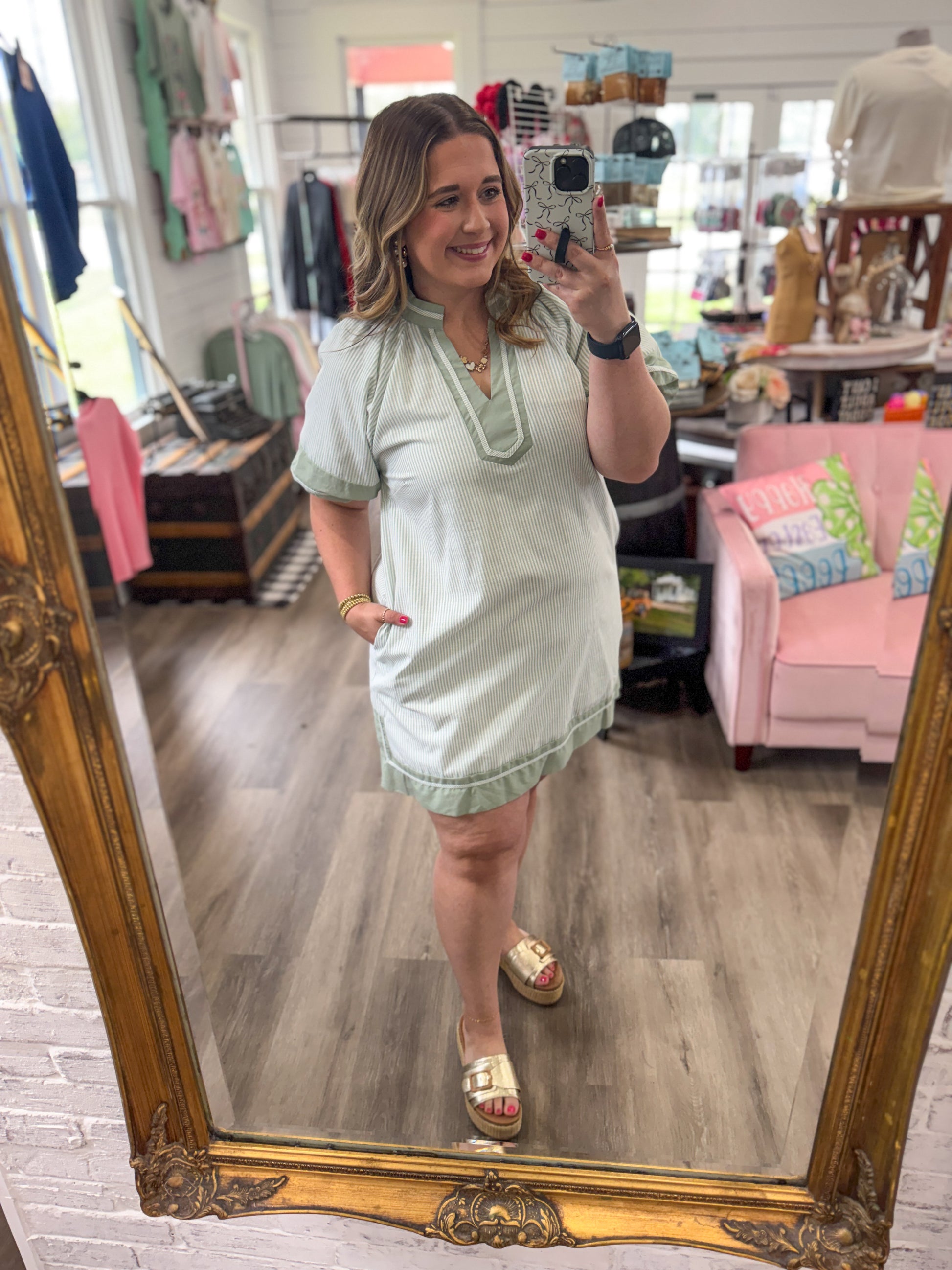 Woman taking a mirror selfie wearing a light green dress in a store.