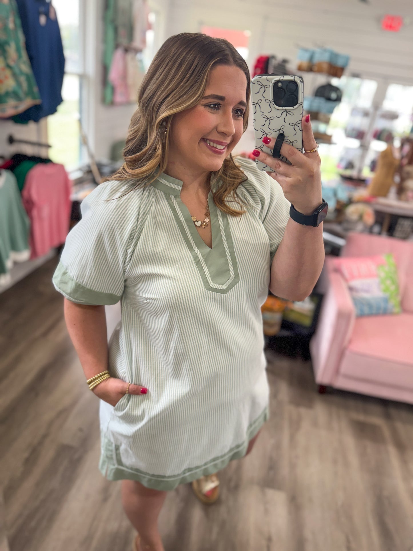 Woman taking a mirror selfie wearing a light green dress in a store.