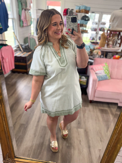 Woman taking a mirror selfie wearing a light green dress in a store.