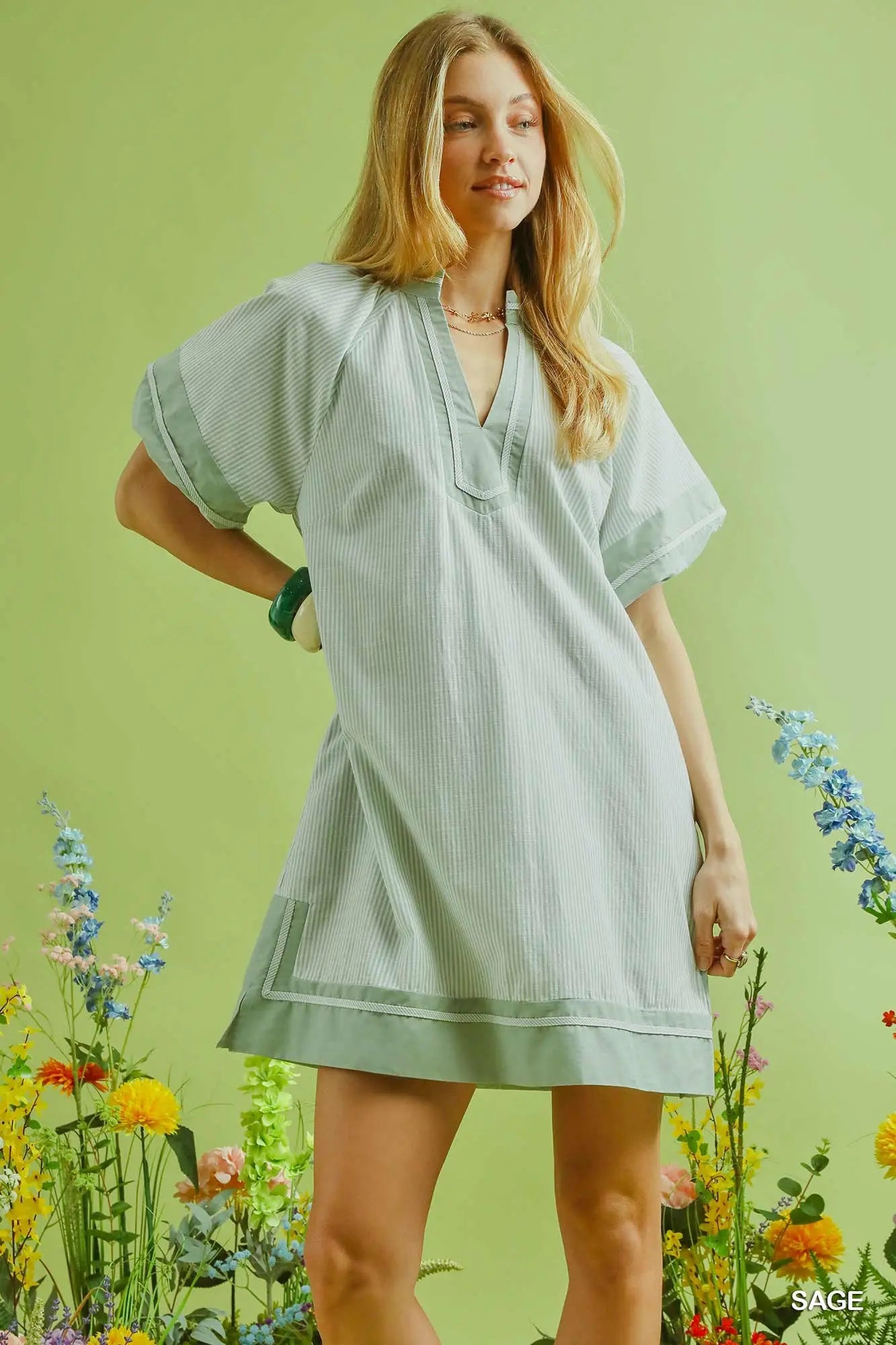 Woman wearing a light green dress standing among flowers with a green background