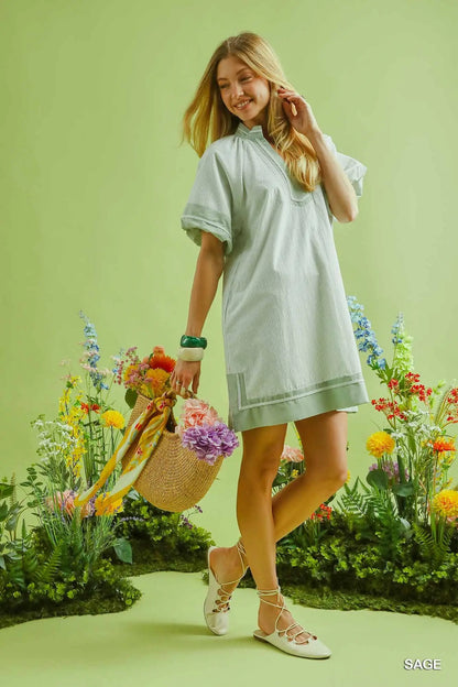 Woman in a light green dress standing among flowers with a green background