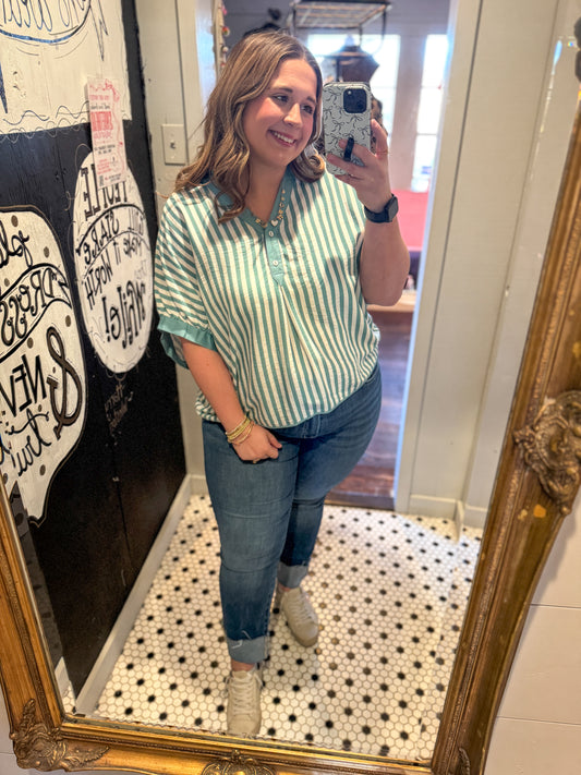 Woman taking a mirror selfie wearing a green and white striped shirt and blue jeans.