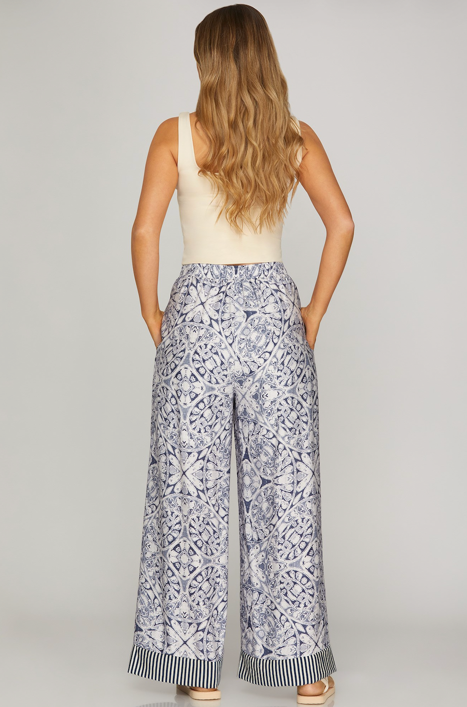 Woman wearing a sleeveless top and patterned pants on a plain background