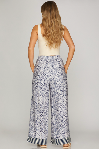 Woman wearing a sleeveless top and patterned pants on a plain background