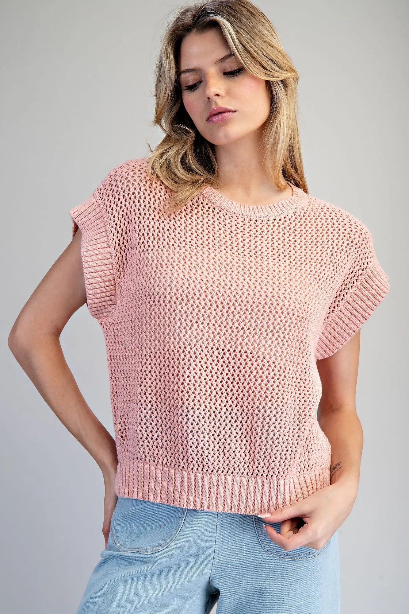 Woman wearing a pink knitted top against a gray background
