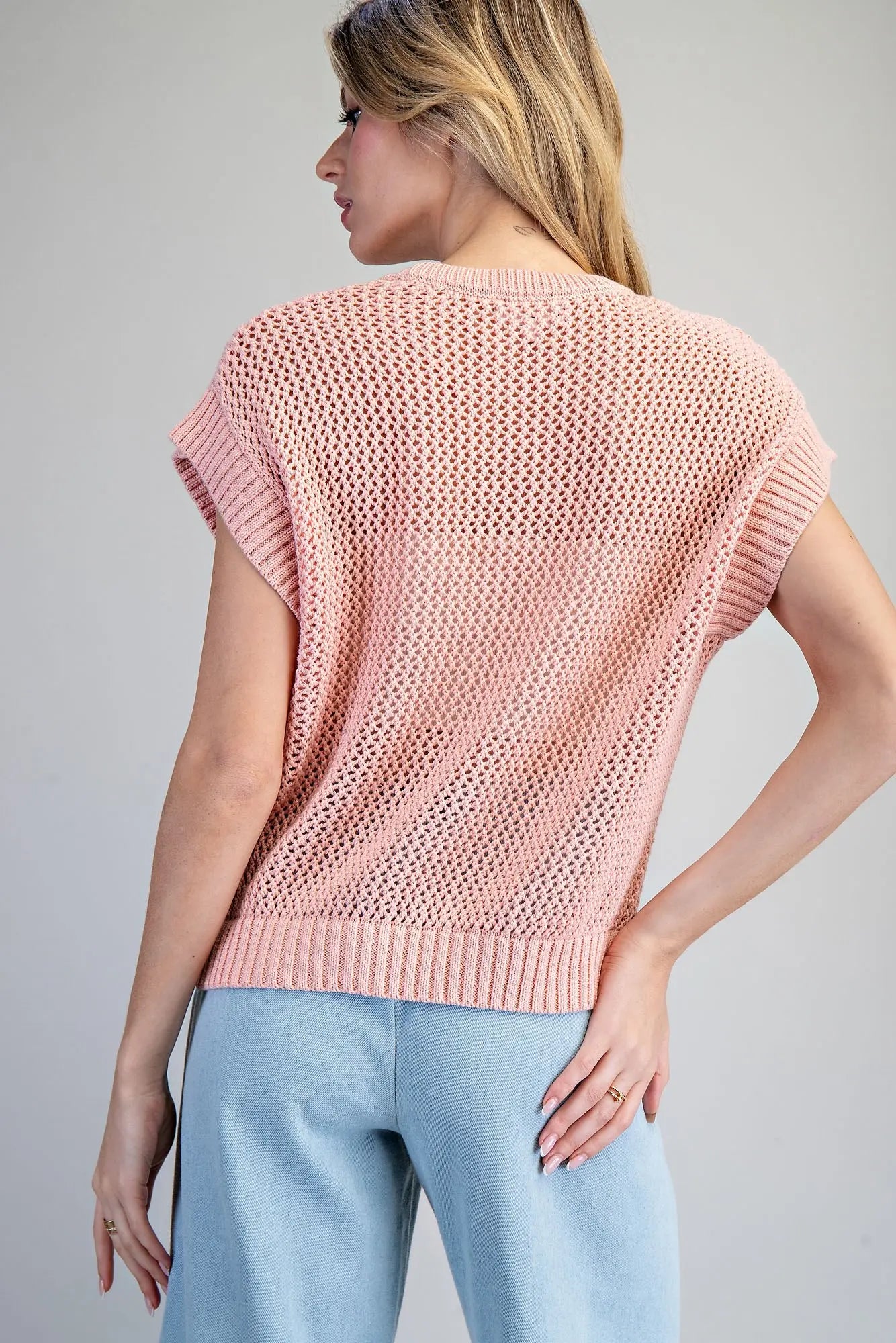 Woman wearing a pink knitted top against a gray background