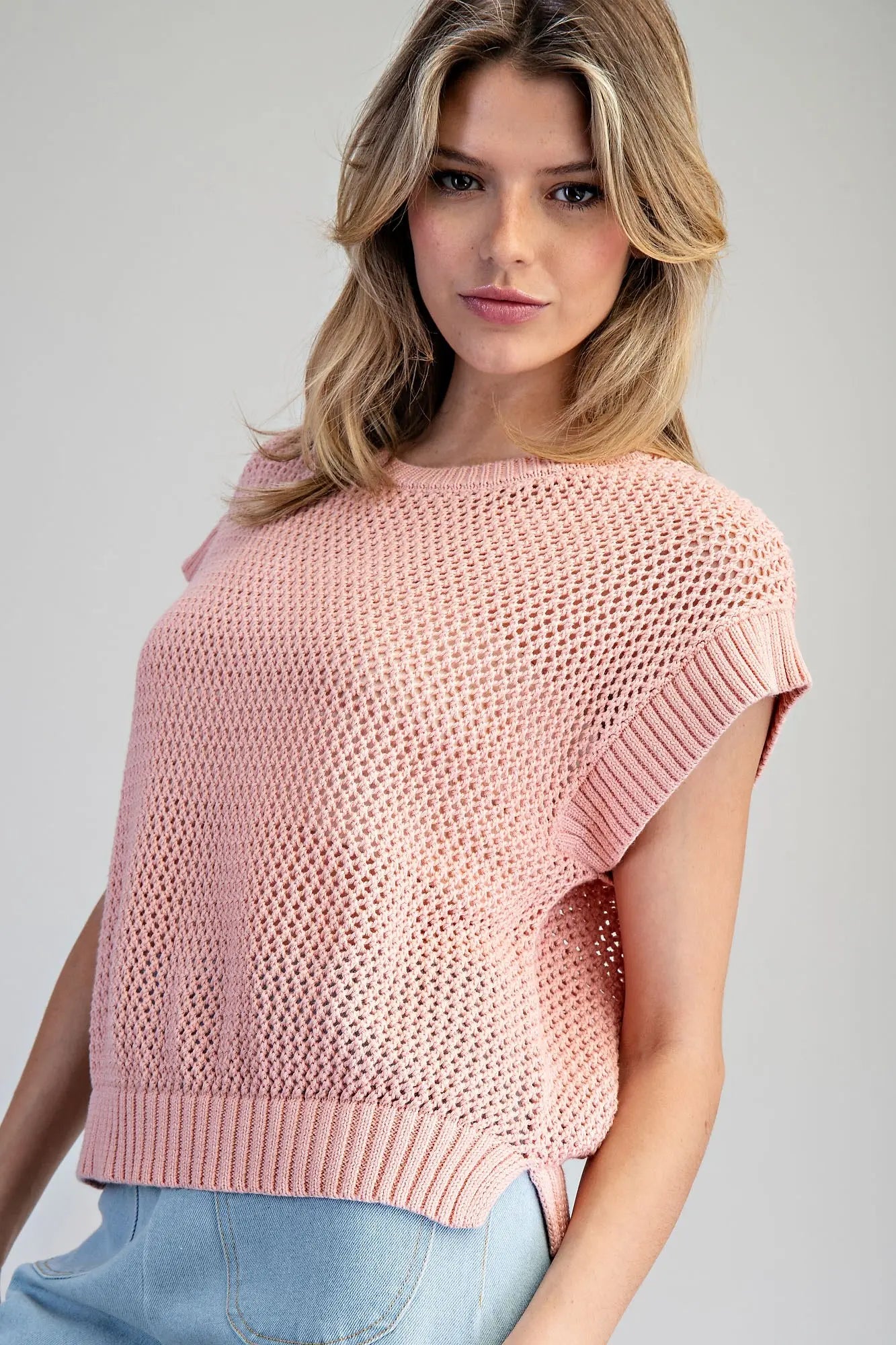 Woman wearing a pink knitted top against a gray background