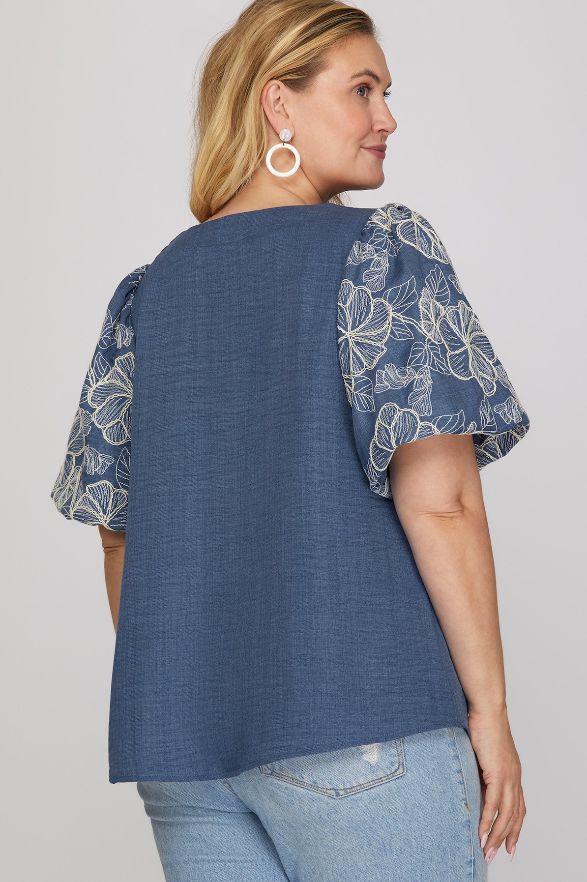 Woman wearing a blue top with floral sleeves on a plain background