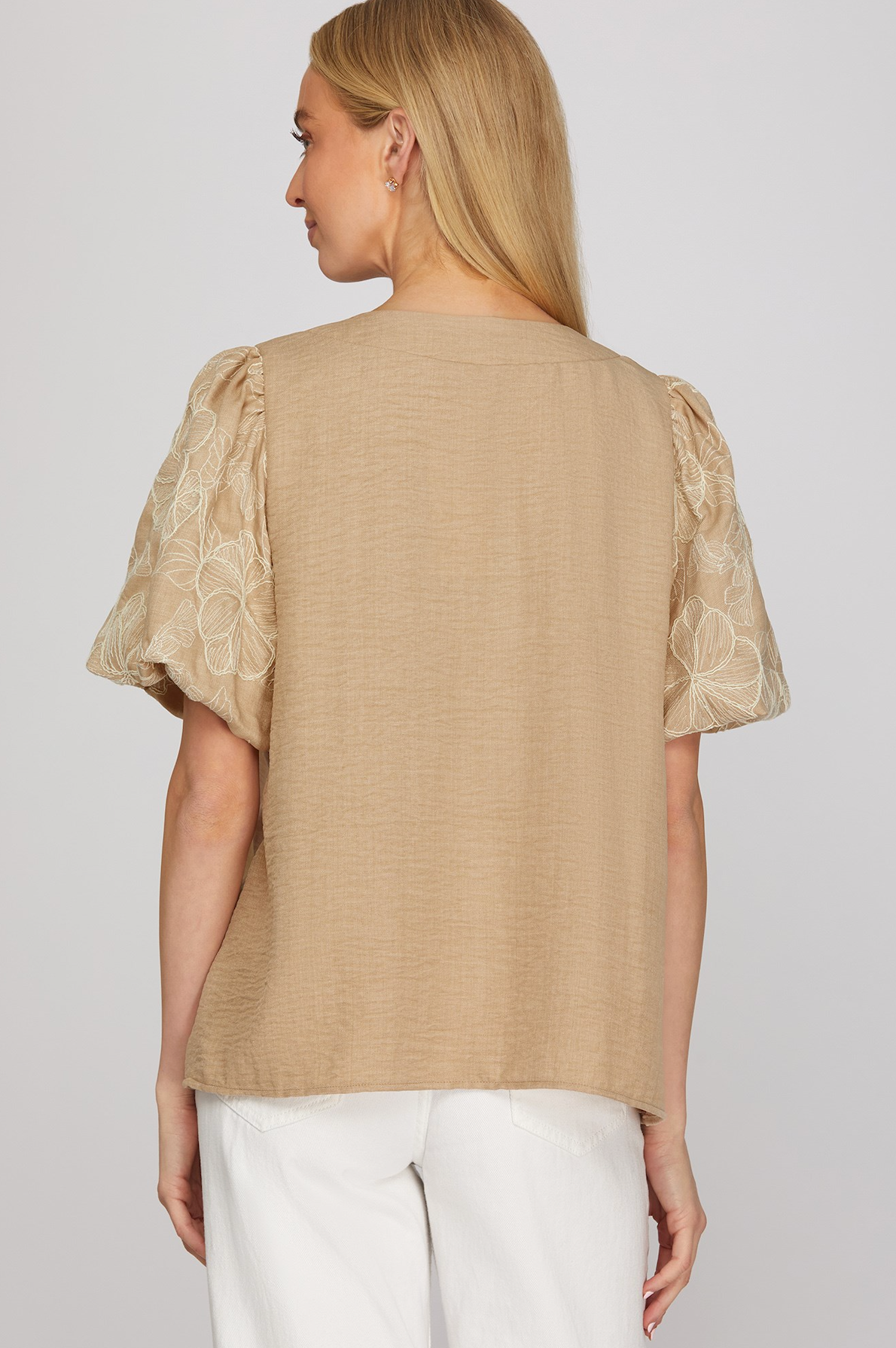 Woman wearing a beige blouse with lace sleeves on a plain background