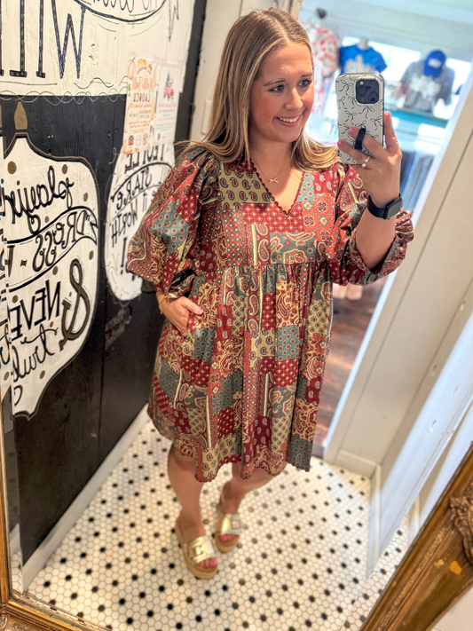 Woman taking a mirror selfie wearing a patterned dress in a room with decorative elements.