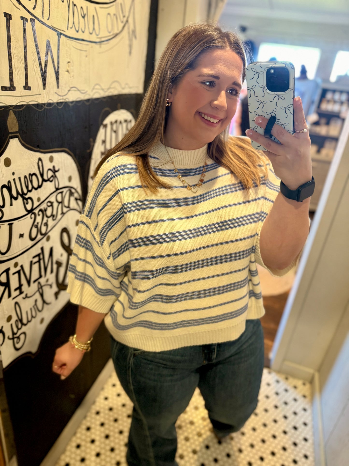 Woman taking a mirror selfie wearing a yellow striped sweater and black pants.