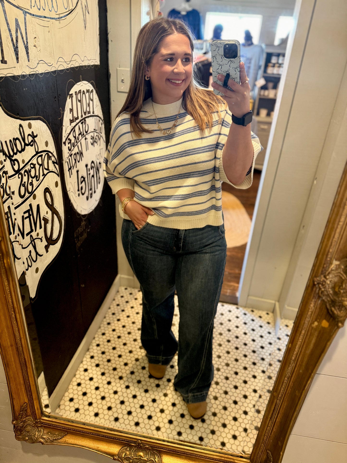Woman taking a mirror selfie wearing a striped sweater and jeans in a room with decorative elements.