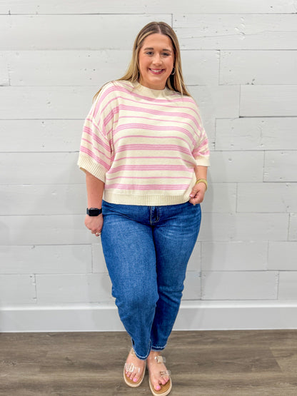 Woman wearing a striped sweater and blue jeans against a white brick wall.