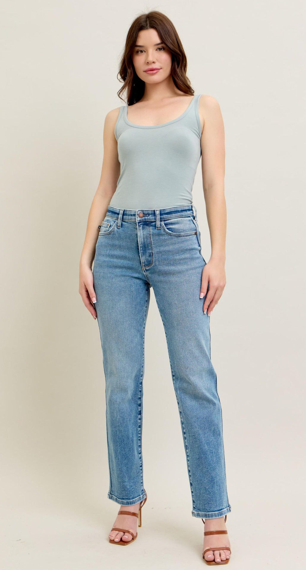Woman wearing a light blue tank top and jeans on a plain background