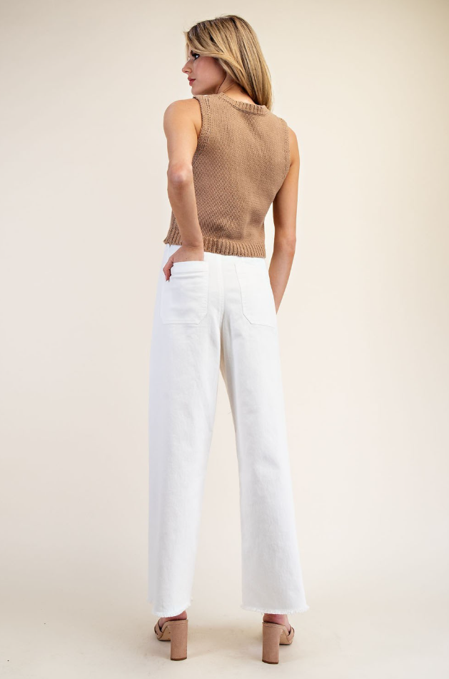 Woman wearing a brown sleeveless top and white pants on a plain background