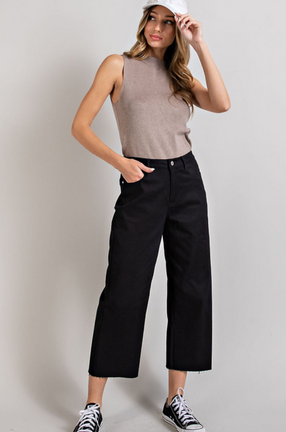 Woman wearing a beige sleeveless top and black pants against a plain background