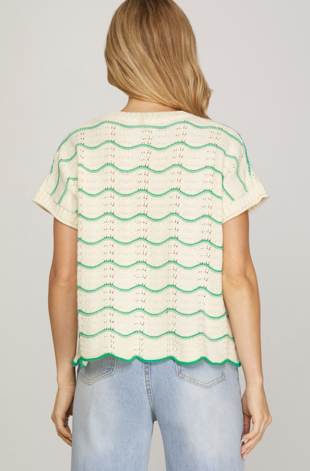 Woman wearing a cream and green patterned top with light blue jeans on a gray background