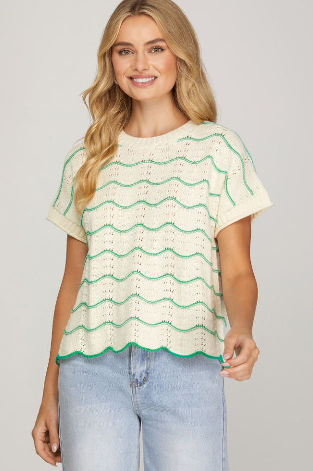 Woman wearing a cream and green patterned top with light blue jeans on a plain background