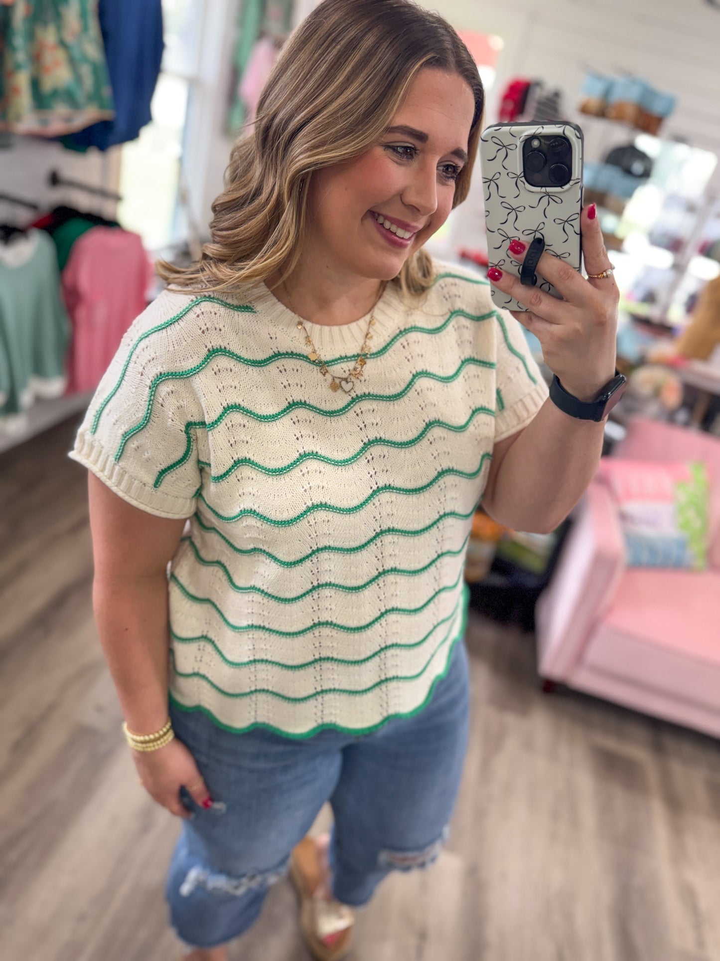 Woman taking a mirror selfie wearing a beige and green striped shirt in a store.