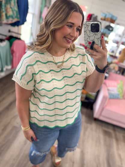 Woman taking a mirror selfie wearing a beige and green striped shirt in a store.