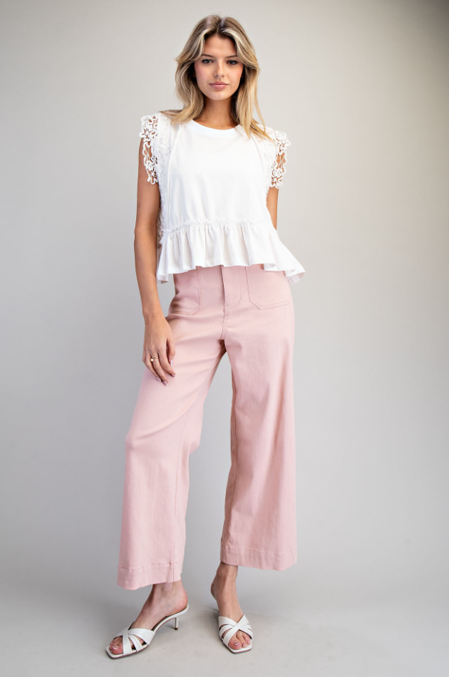 Woman wearing a white top with lace details and pink pants on a gray background
