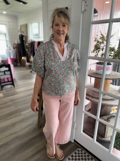 Woman standing in a store wearing a floral blouse and pink pants.