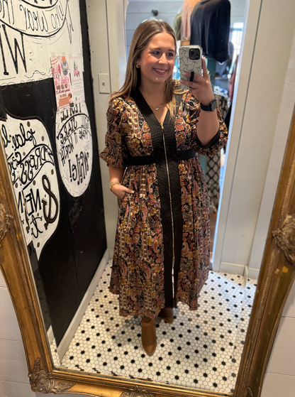 Woman taking a mirror selfie wearing a patterned dress in a room with decorative elements.